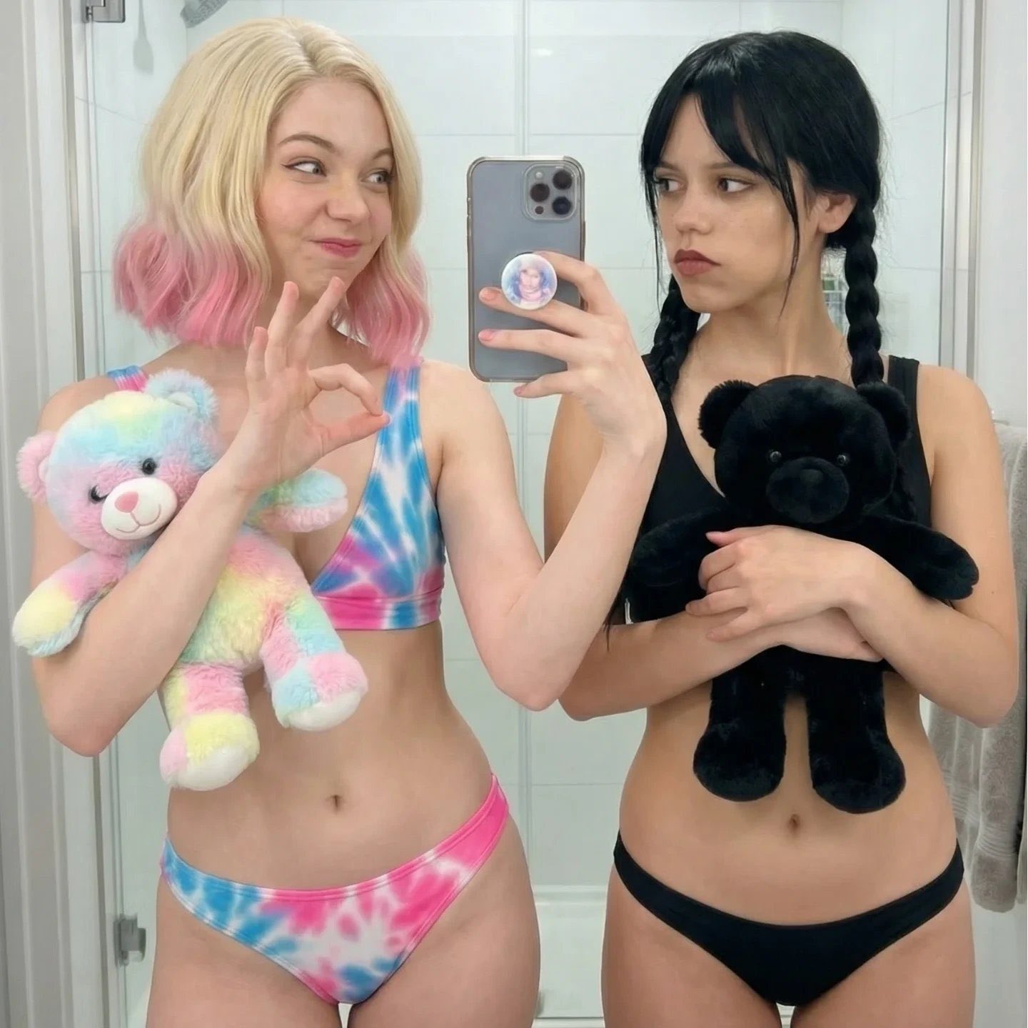 Two women resembling Emma Myers and Jenna Ortega in Wednesday and Enid cosplay, taking a mirror selfie while holding teddy bears.