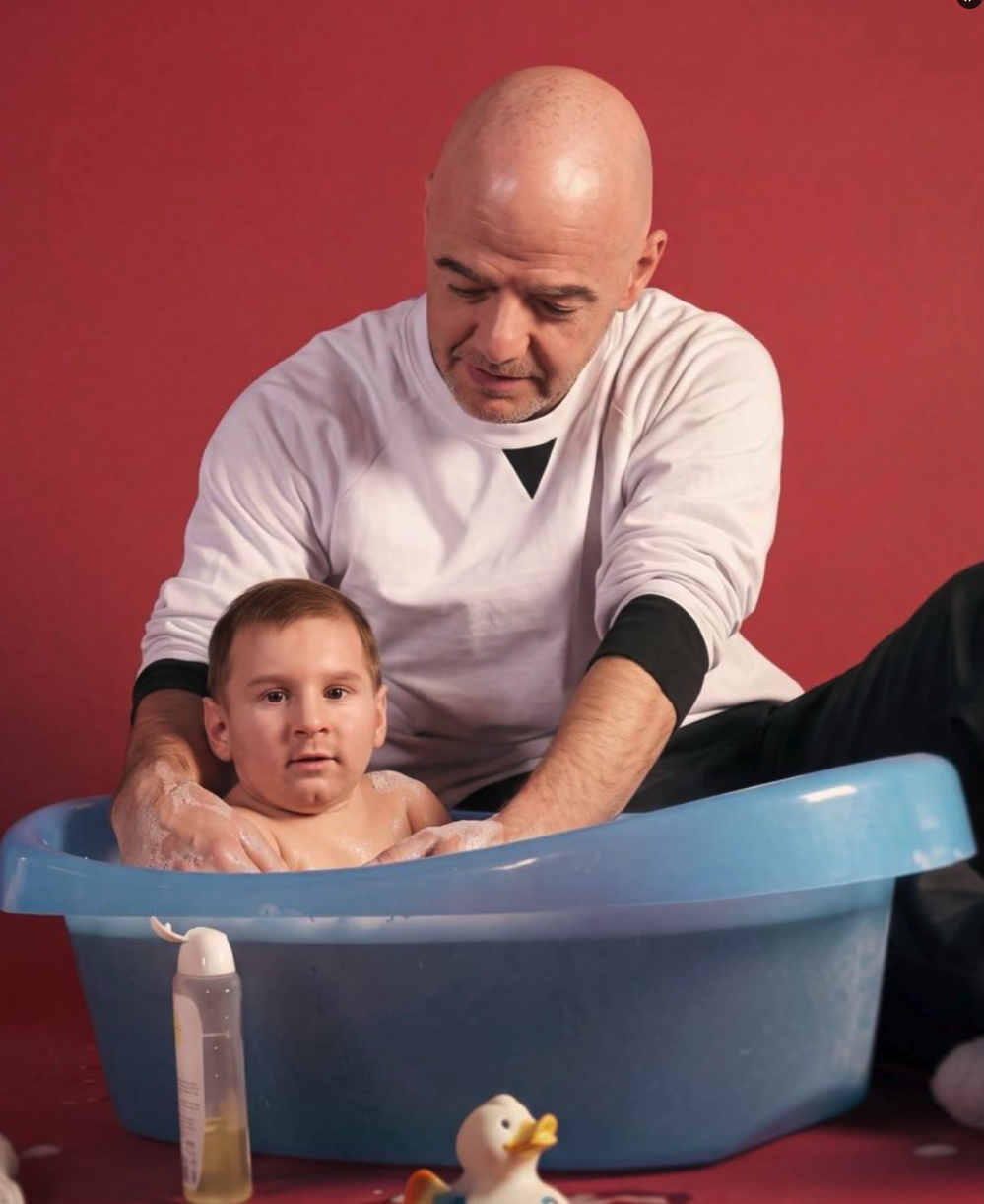 An adult in a white long-sleeve shirt bathing a young child in a blue plastic tub against a red background.
