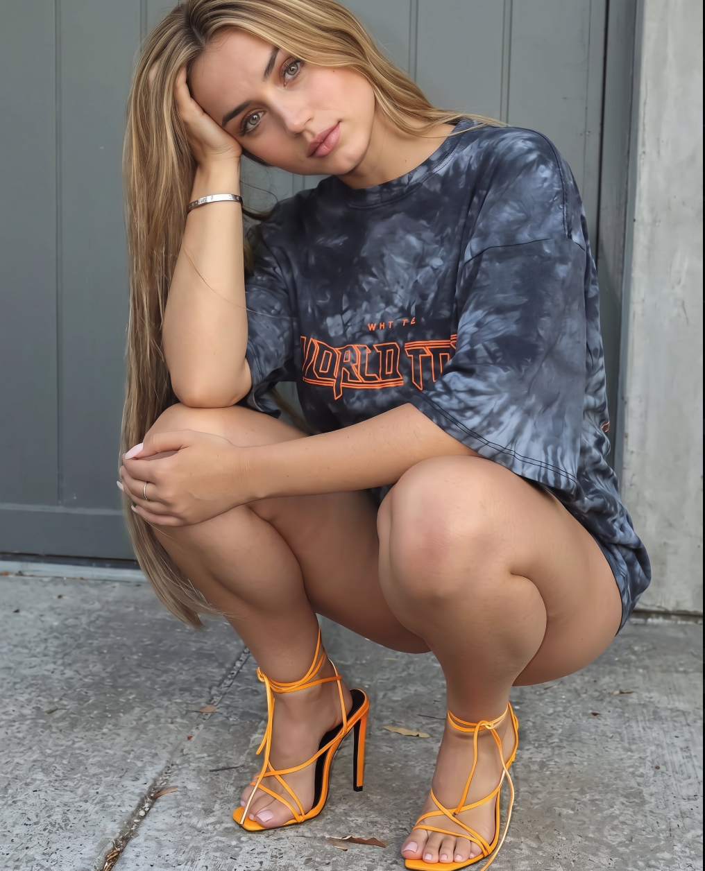 A woman resembling Ana de Armas squatting outdoors in a tie-dye t-shirt and orange strappy heels.