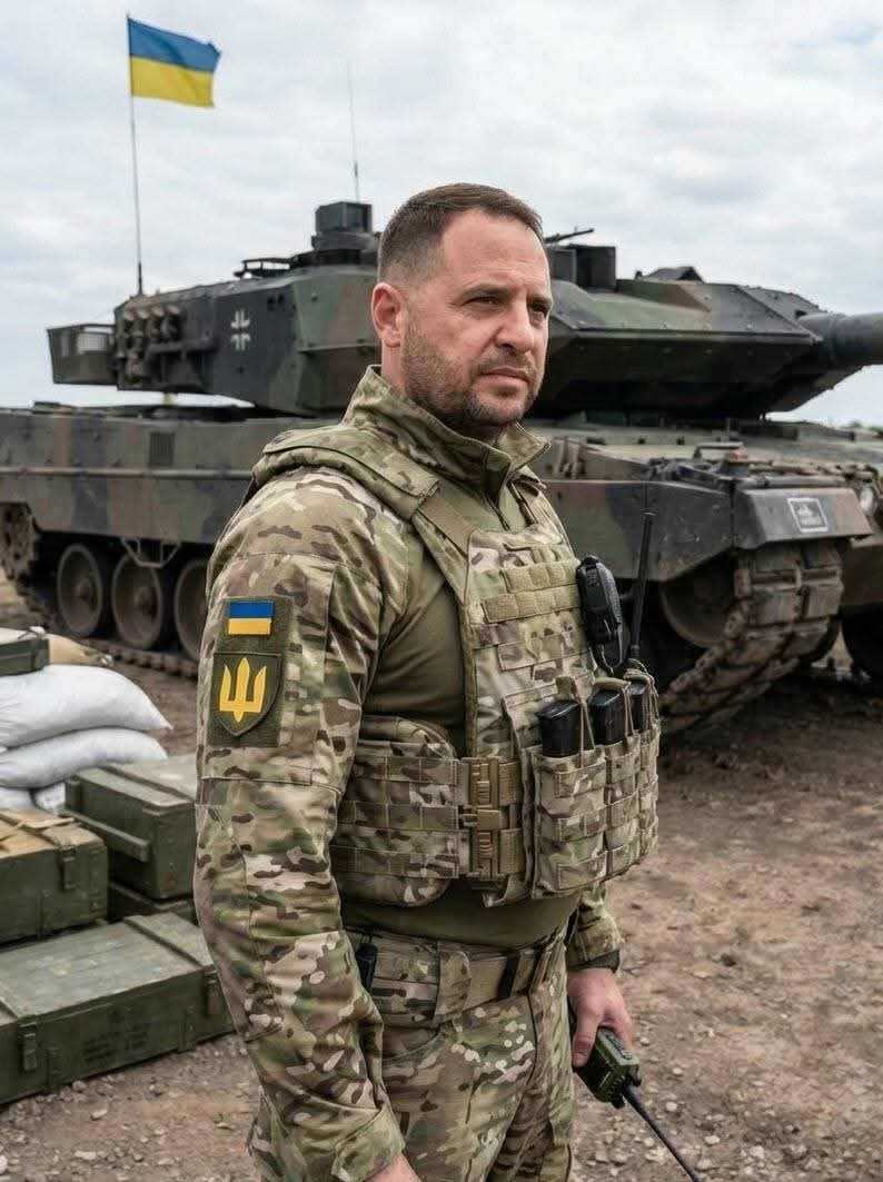 A man resembling Andriy Yermak in Ukrainian camouflage uniform standing in front of a tank with a Ukrainian flag.