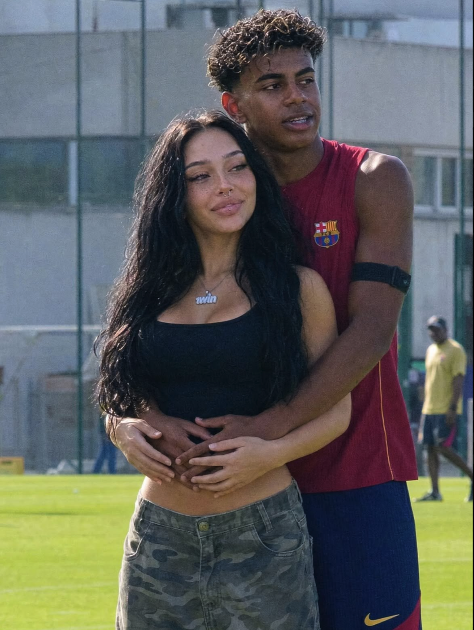 Lamine Yamal in a Barcelona training jersey embracing a young woman on a soccer training pitch.