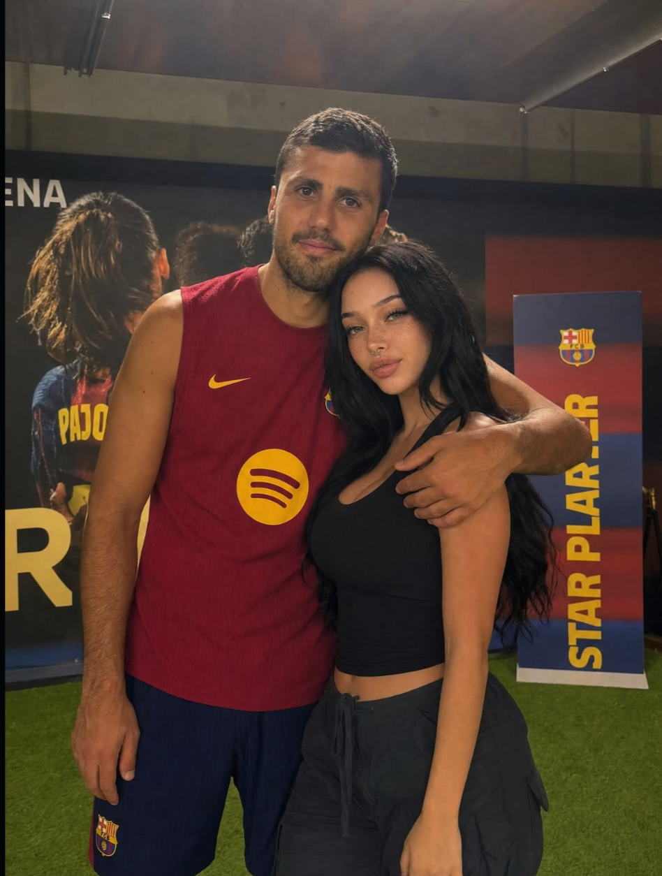 A man in a Barcelona FC training kit posing with a dark-haired woman at an indoor club event.