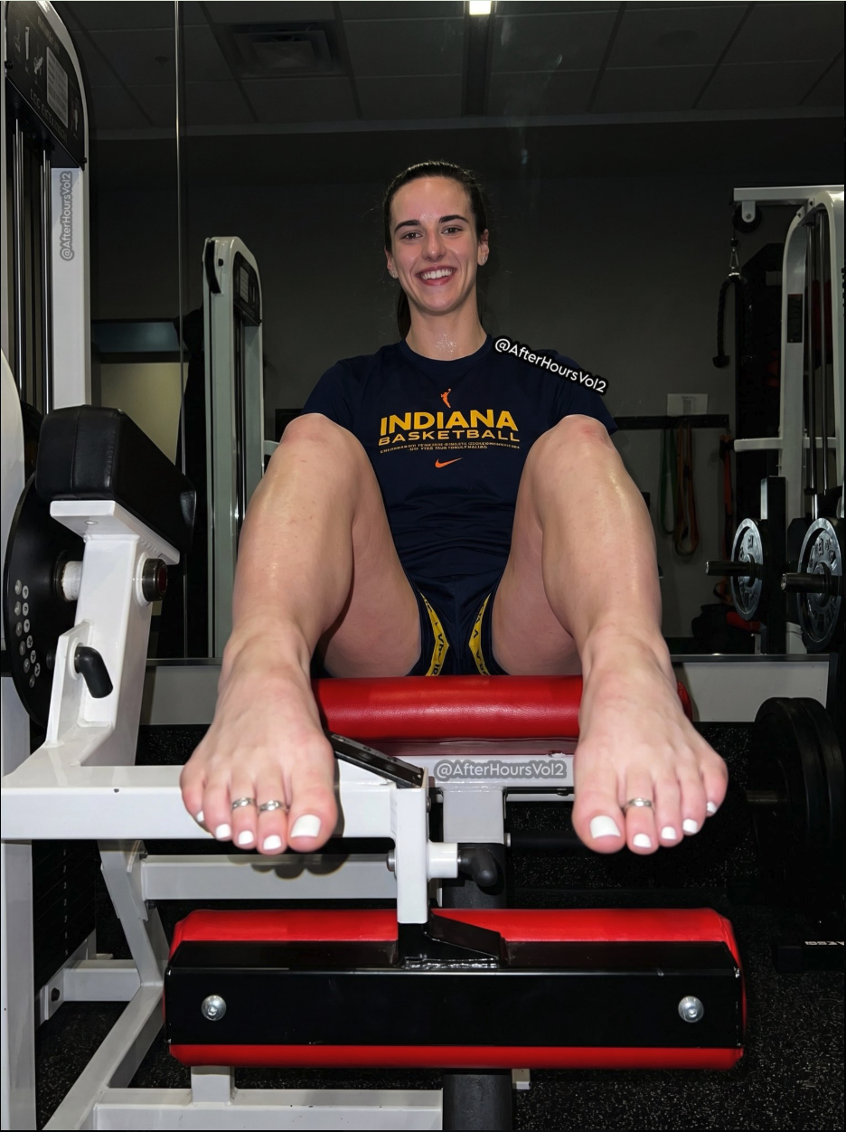 A woman resembling Caitlin Clark seated on a gym machine in an Indiana Basketball shirt, smiling and barefoot.