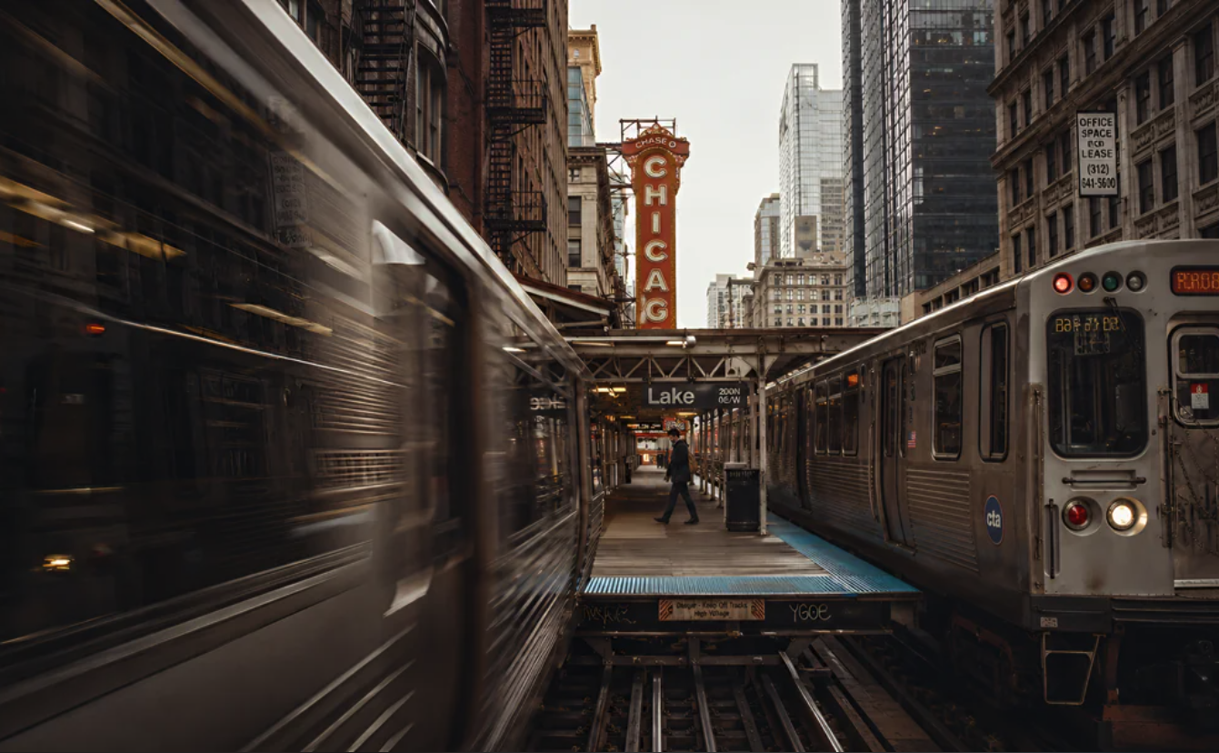 An elevated train platform with 'Lake / 200 N' signage between two CTA trains, with the vertical Chicago Theatre marquee in the background.
