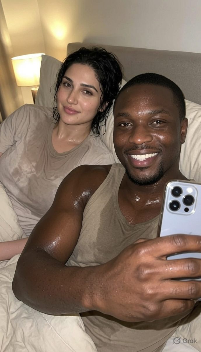 A man and woman lying in bed taking a selfie together, both appearing sweaty and smiling at the camera.