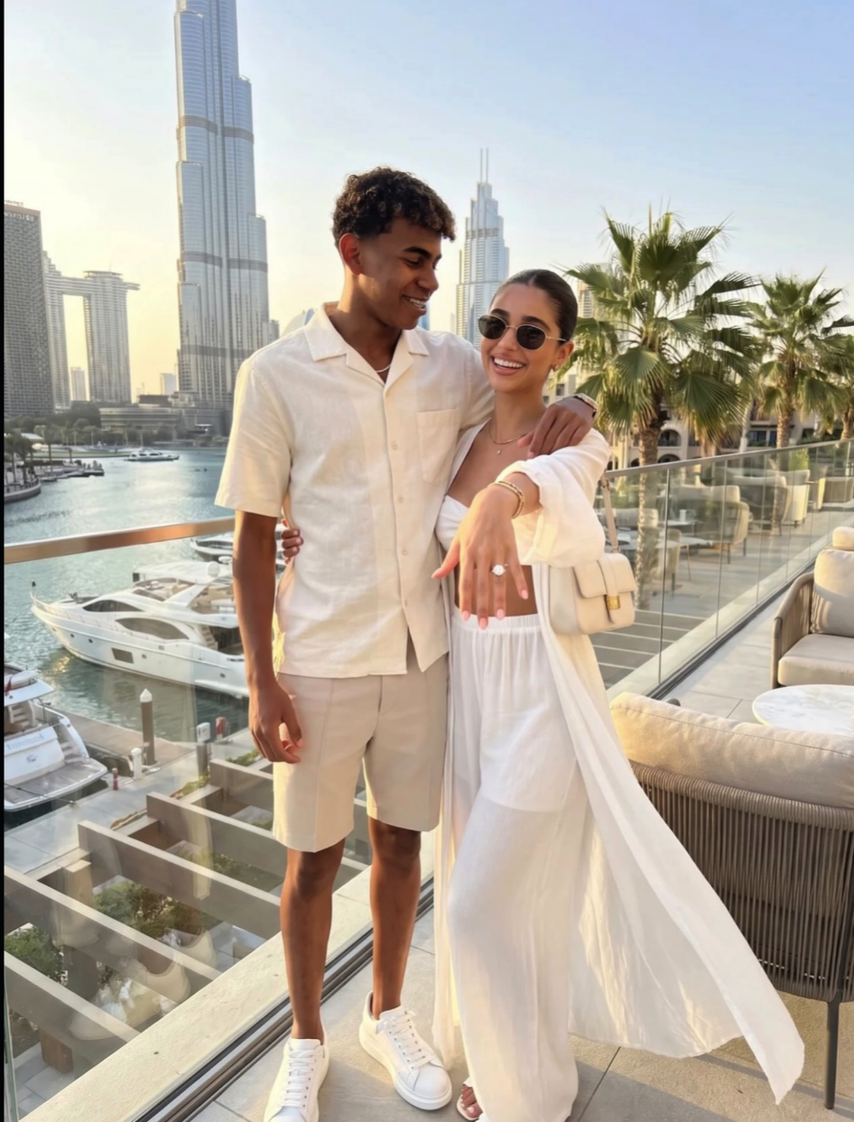 A young man and woman in white clothing posing together on a terrace overlooking the Dubai skyline and marina.