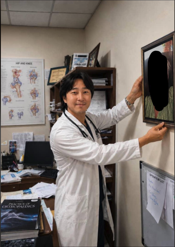 A man in a white medical coat with a stethoscope hanging a framed picture in an orthopedic office.