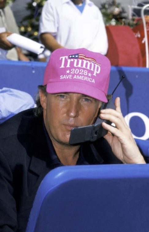 A man resembling Donald Trump wearing a pink 'Trump 2028 Save America' cap and holding an older-model mobile phone to his ear.