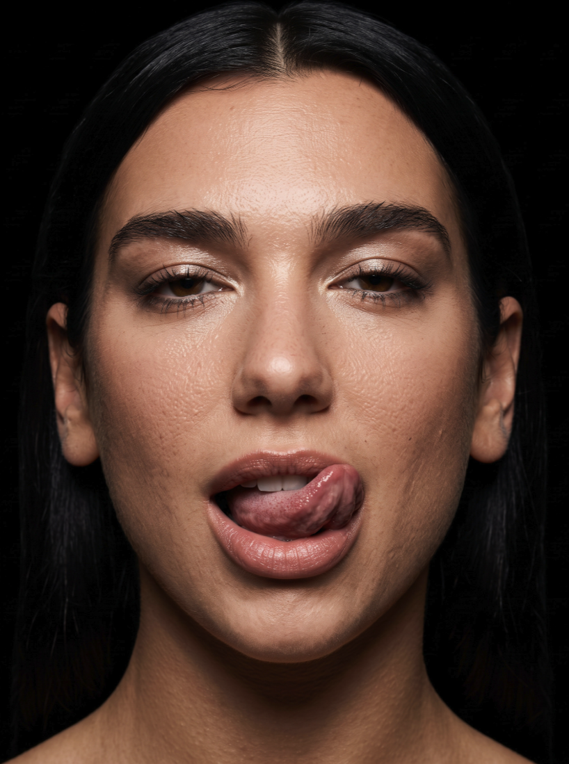 A close-up portrait of a woman resembling Dua Lipa with dark hair against a black background.