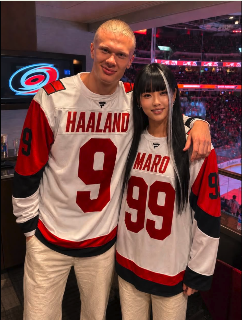 A man resembling Erling Haaland and a woman in matching Carolina Hurricanes jerseys at an indoor arena.