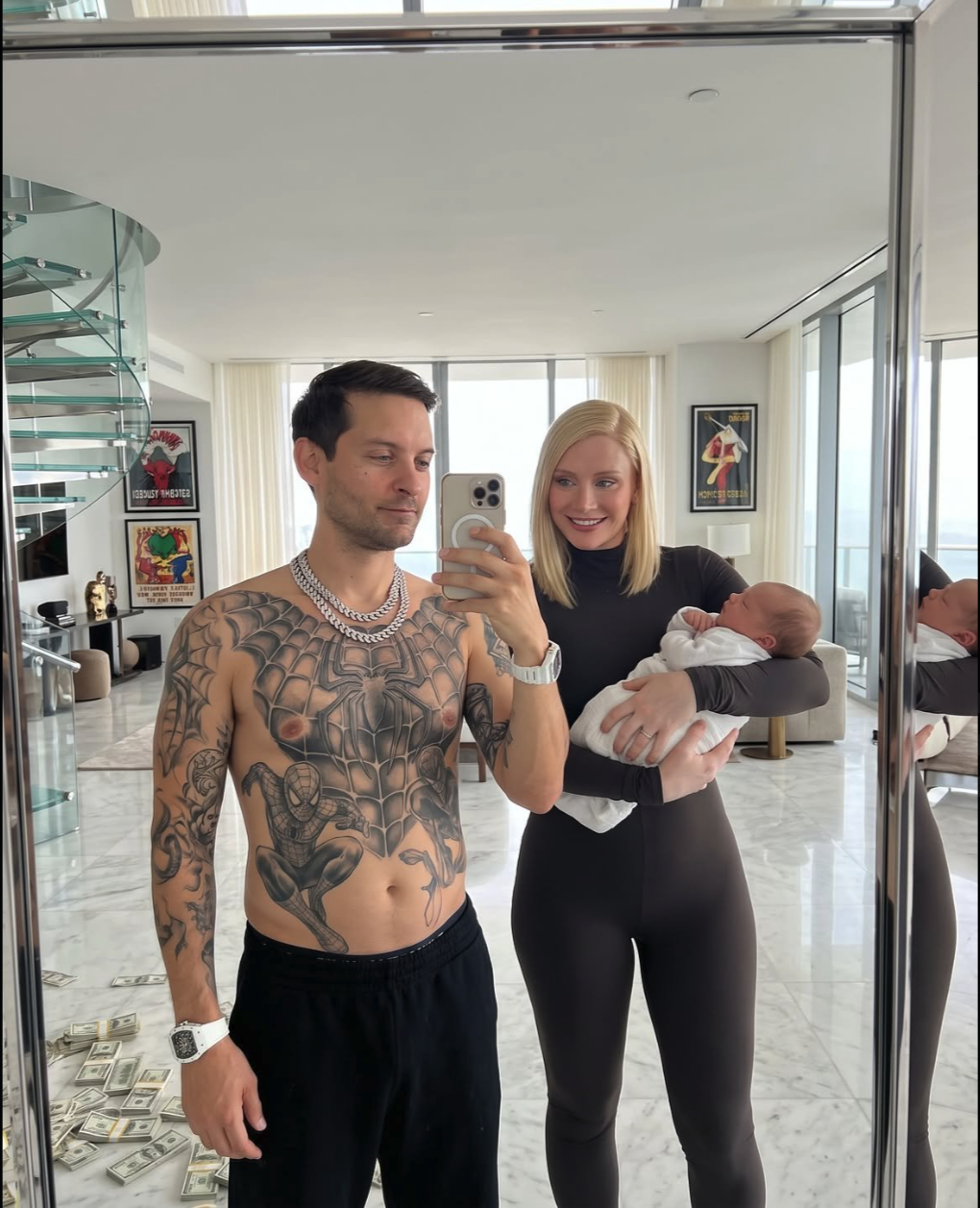 A shirtless man with a chest tattoo and a woman holding a swaddled baby take a mirror selfie in a luxury apartment.
