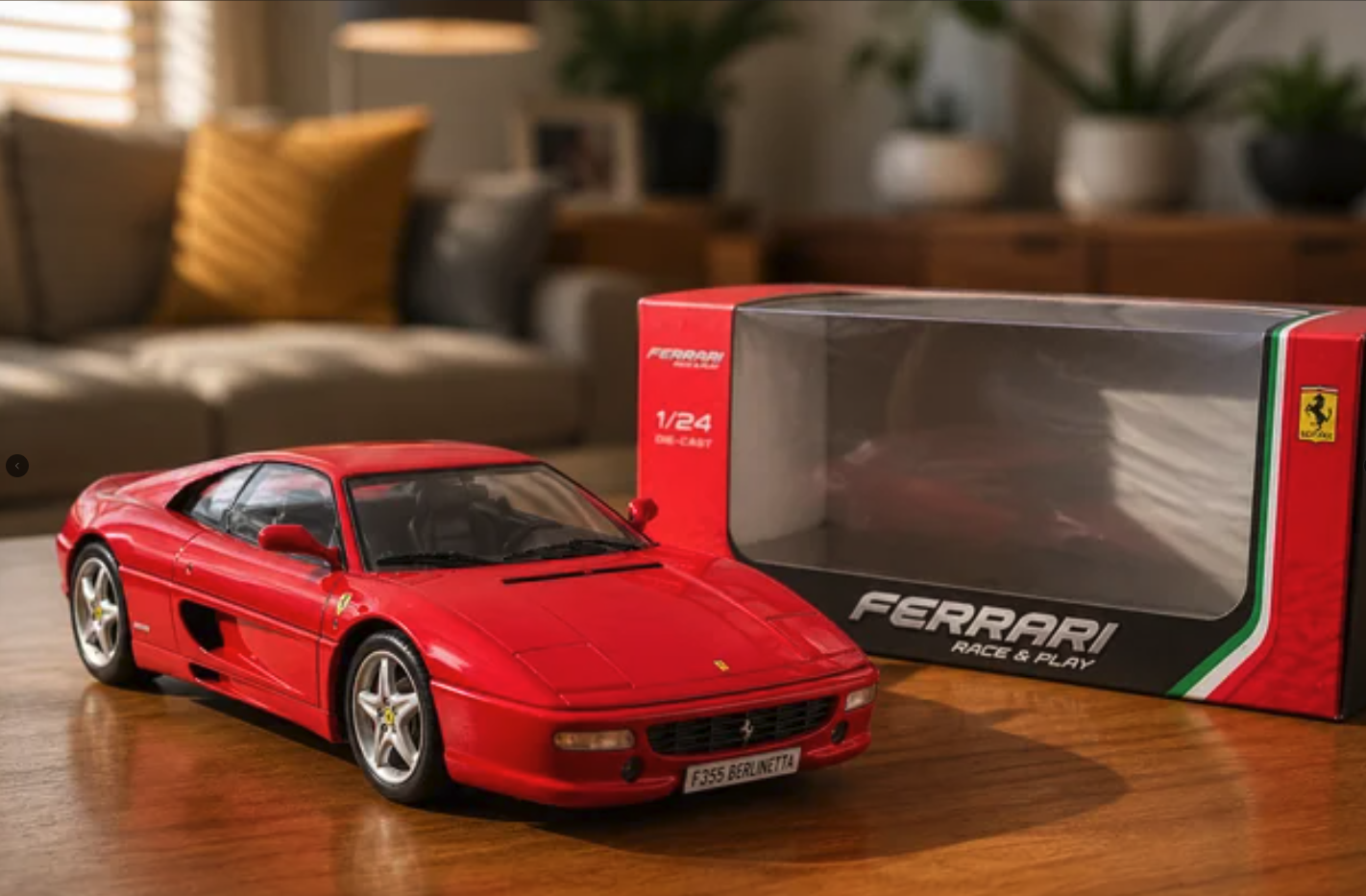 A red Ferrari F355 Berlinetta 1/24 scale die-cast model car next to its branded packaging box on a wooden table.