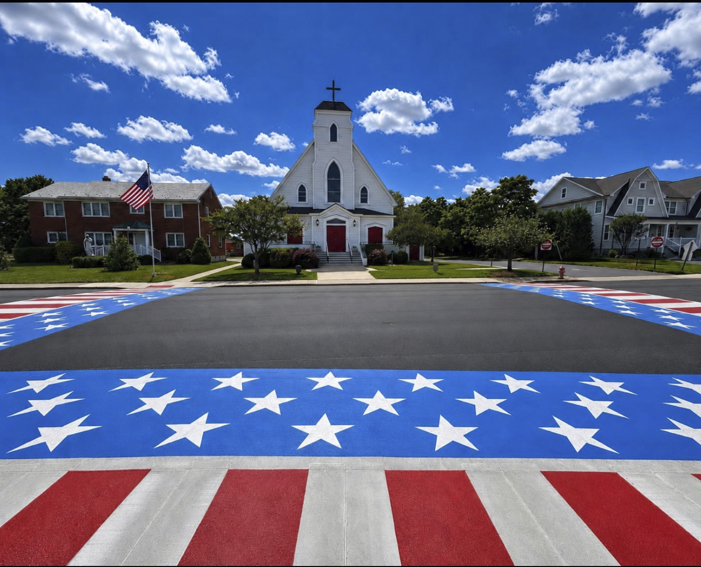 A small white church with a steeple beside an American flag, fronted by a street painted in stars and stripes.