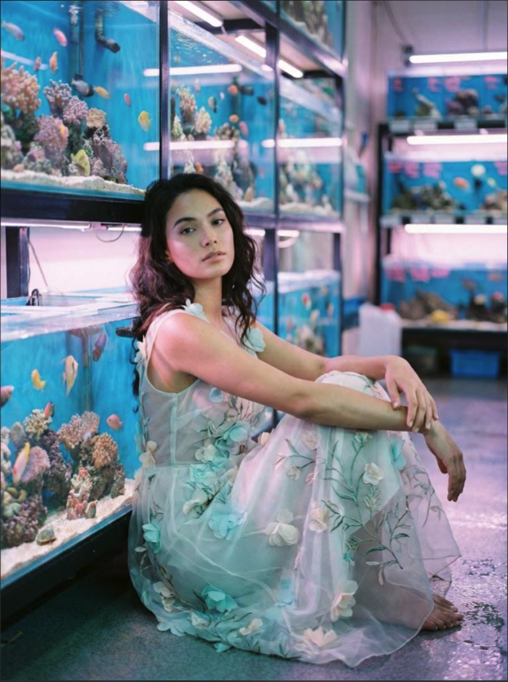 A woman seated on the floor of an aquarium store in a floral dress.