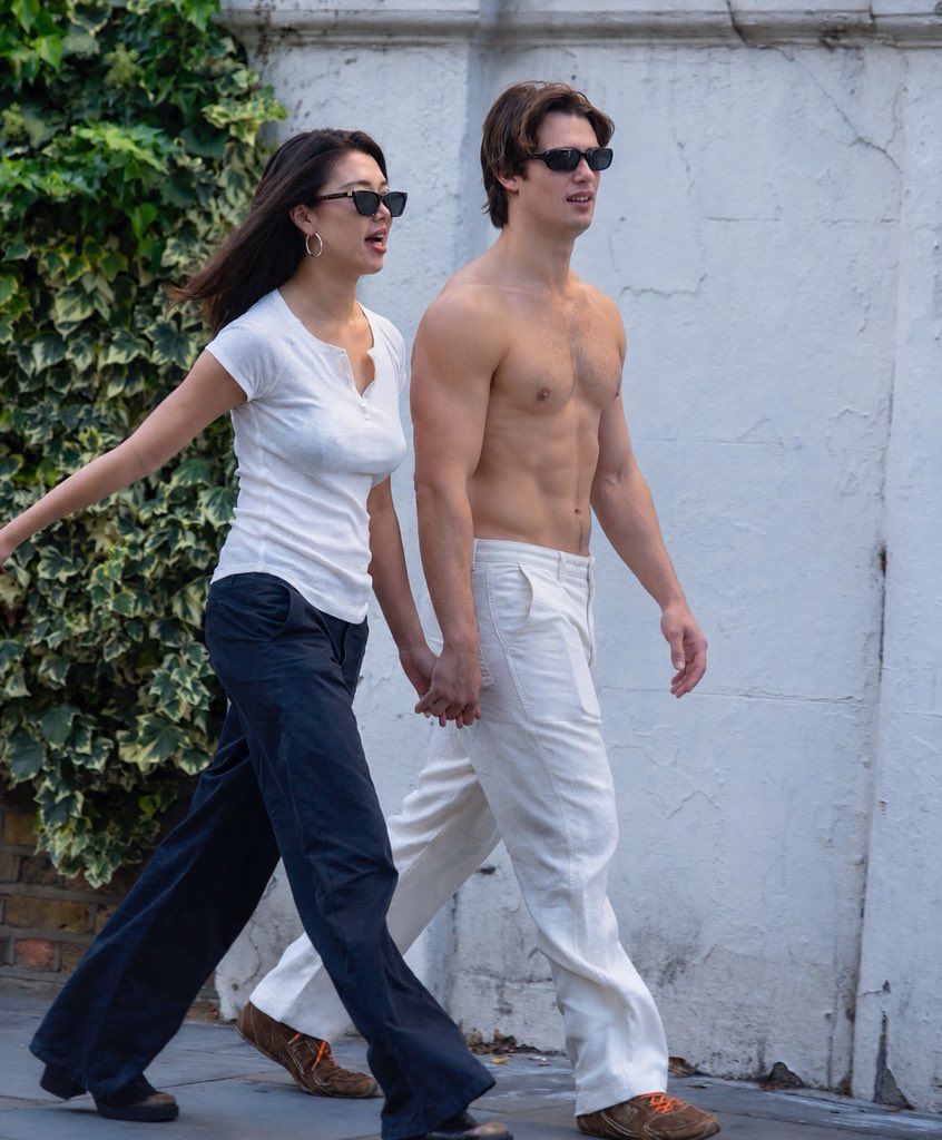 A man resembling Nicholas Galitzine, shirtless, walking alongside Cameron Valentina Eyre on a sidewalk.