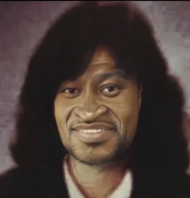 A portrait of a man resembling george floyd with long dark hair against a softly lit studio background.