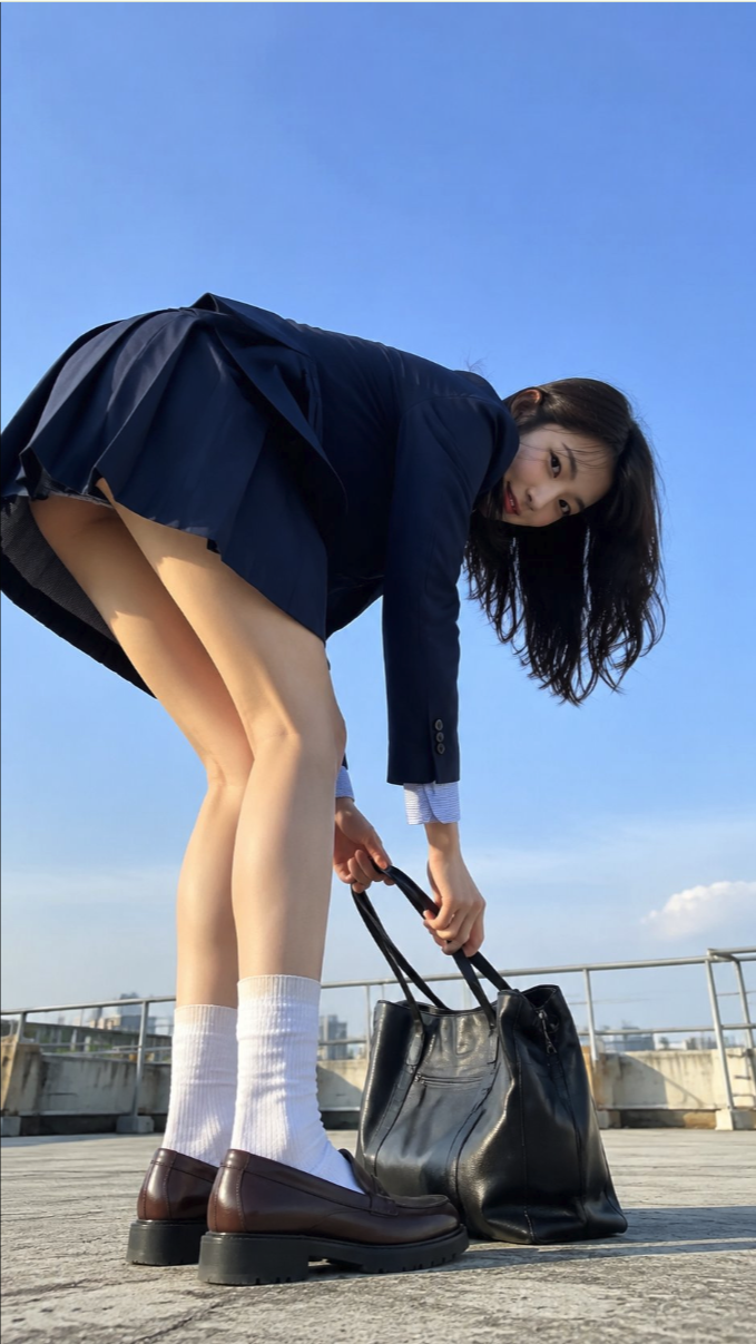 A woman bending forward while holding a black tote bag on a rooftop.