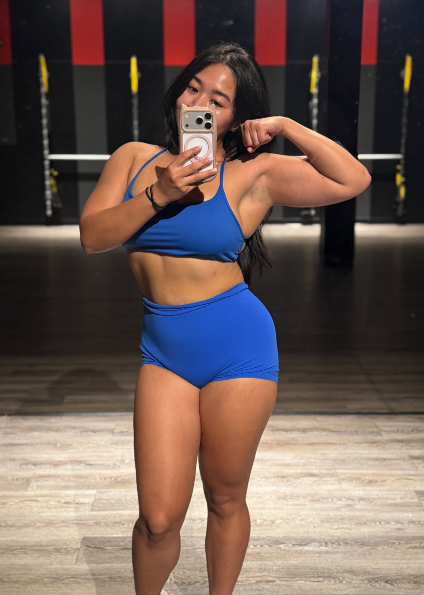 A mirror selfie appearing to show a woman in a blue athletic outfit posing at a gym.