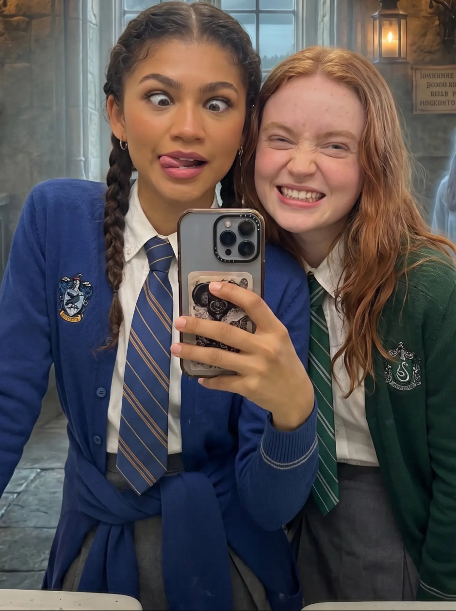 Zendaya and Sadie Sink in Hogwarts-style school uniforms taking a selfie in a stone interior.