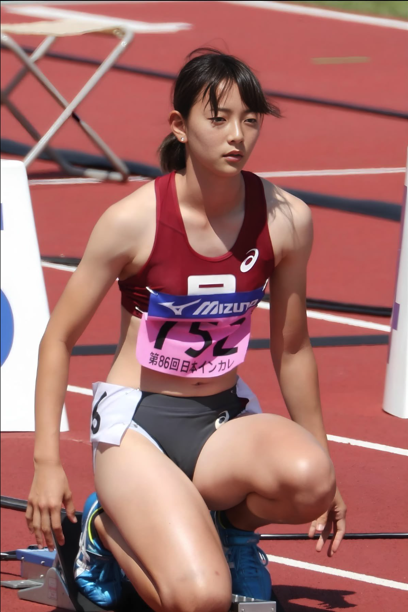 A young woman in athletic wear crouched in starting position on a red running track, with bib 752.