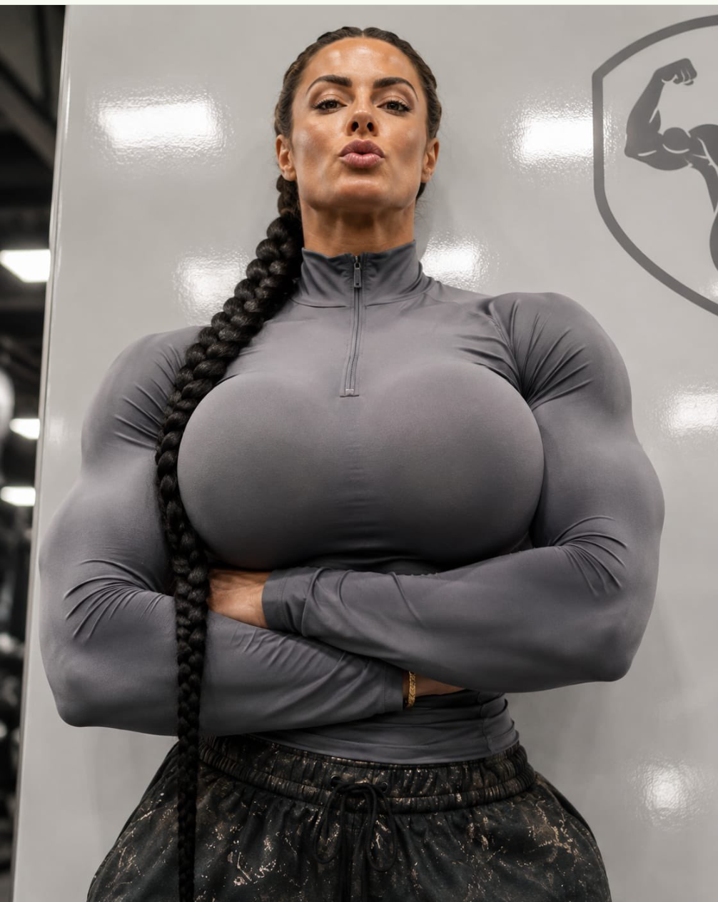 A muscular woman posing with crossed arms in a tight gray athletic top.
