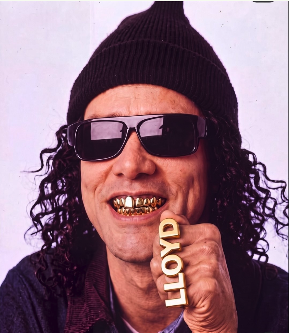 A man resembling Jim Carrey wearing a black beanie, dark sunglasses, and gold grillz, holding a gold knuckle ring reading 'LLOYD'.