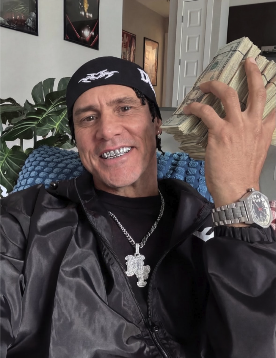 A man resembling Jim Carrey wearing a black bandana cap and pendant necklace, holding a stack of cash indoors.