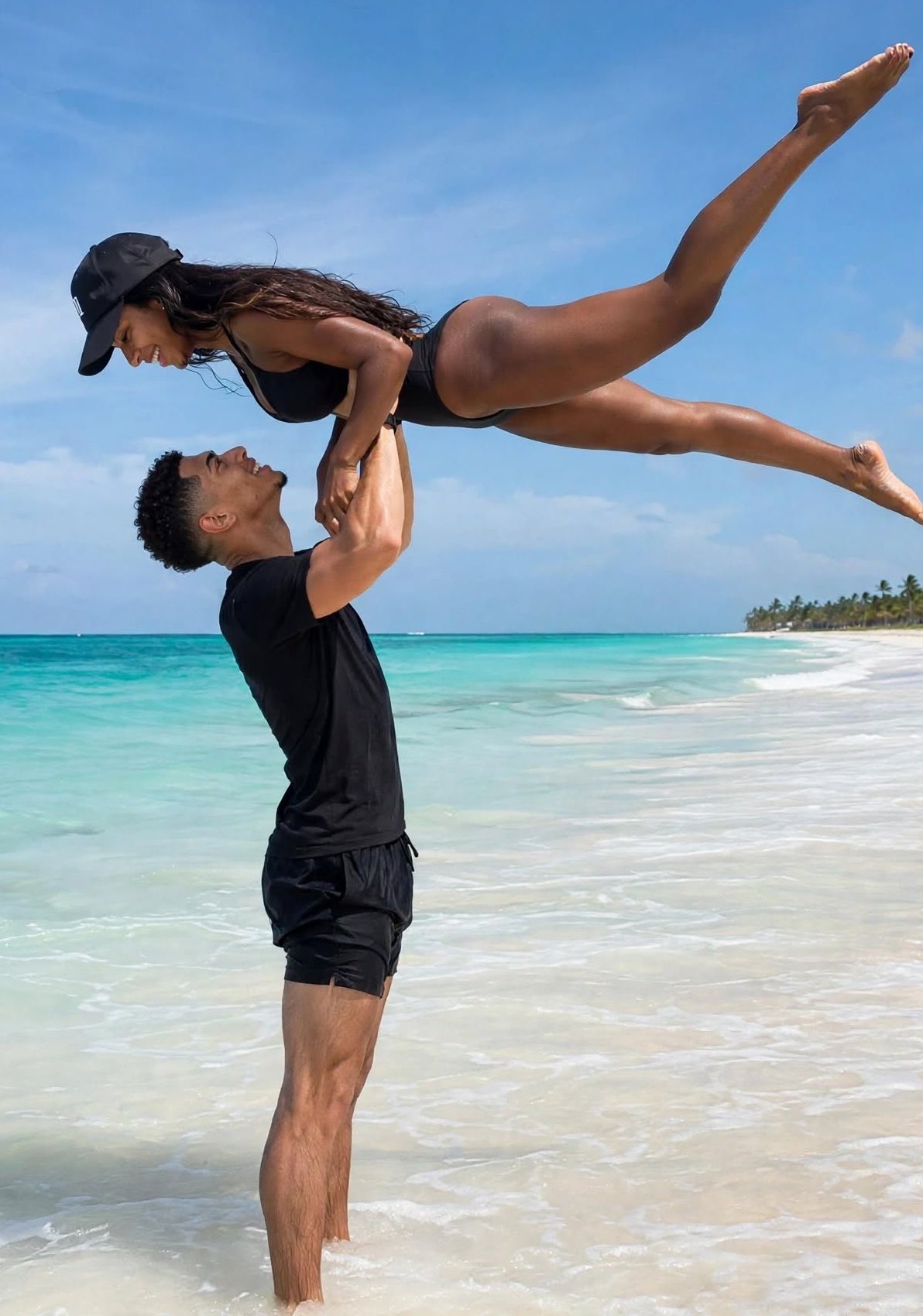 A man resembling Jude Bellingham lifting a woman resembling Ashlyn Castro horizontally in the air on a tropical beach.