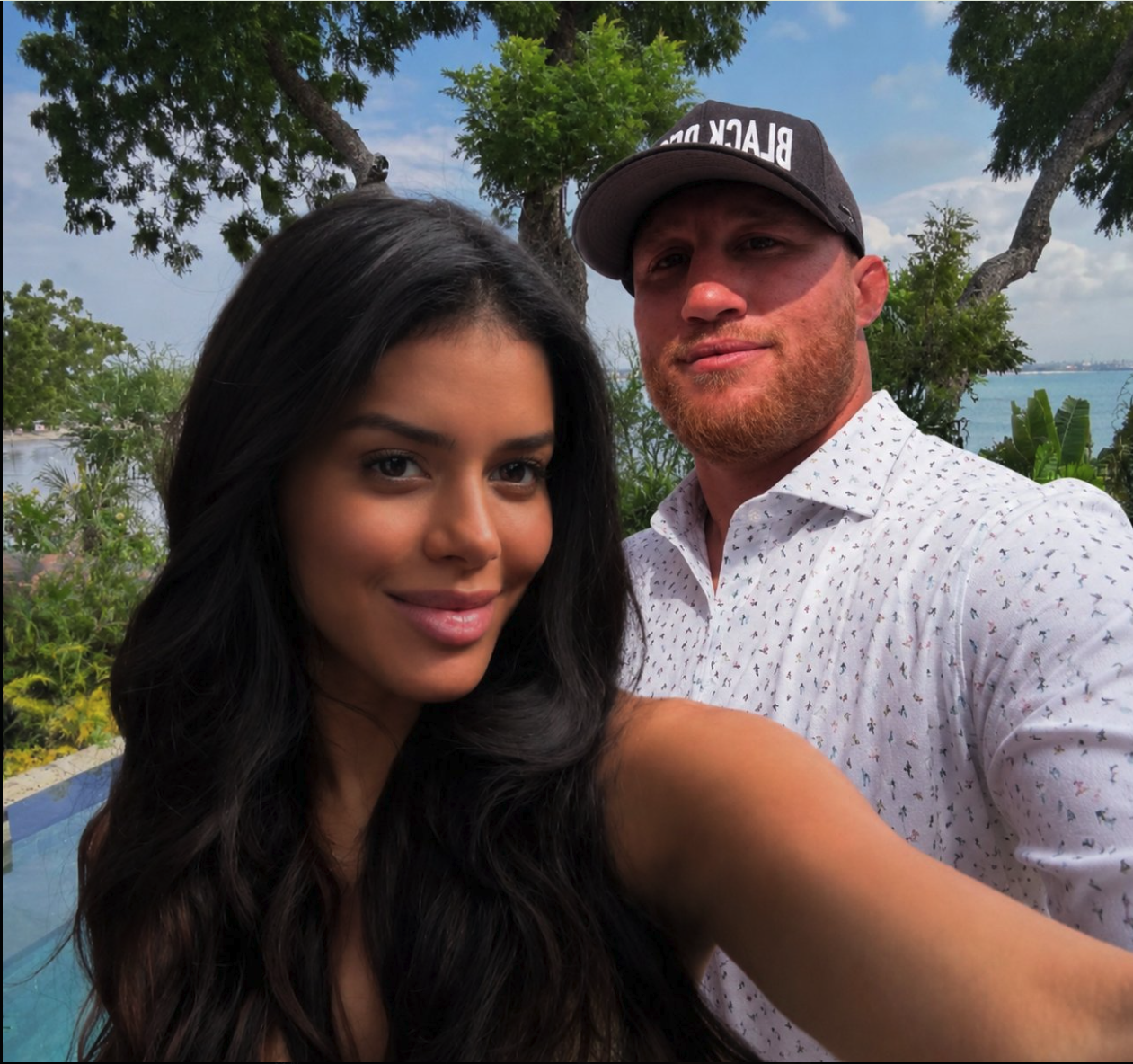 A close-up selfie of a man resembling Justin Gaethje and a woman posing together outdoors, with a pool and water visible behind them.