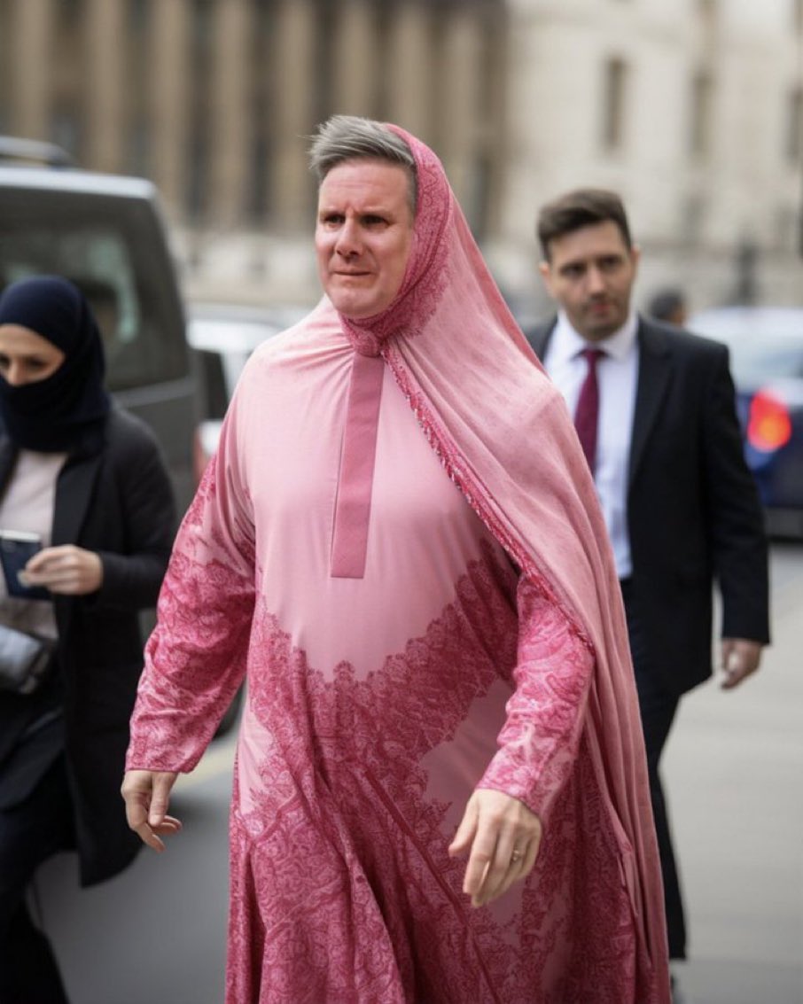 A man resembling Keir Starmer wearing a sheer pink hooded robe with lace detailing, walking outdoors.
