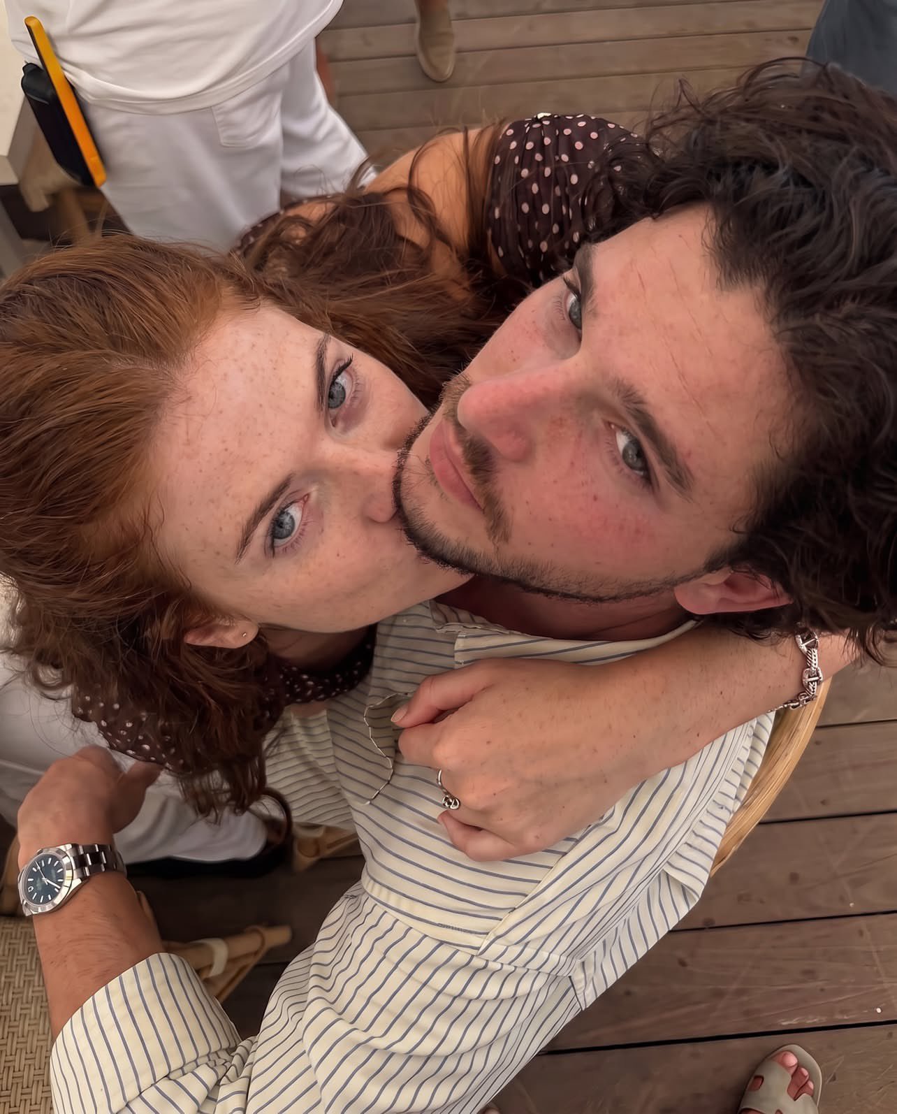 A man and a woman resembling Kit Harington and Rose Leslie embracing while seated at an outdoor table.