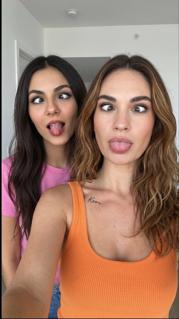 Two women resembling Lily James and Victoria Justice taking a selfie while sticking their tongues out indoors.