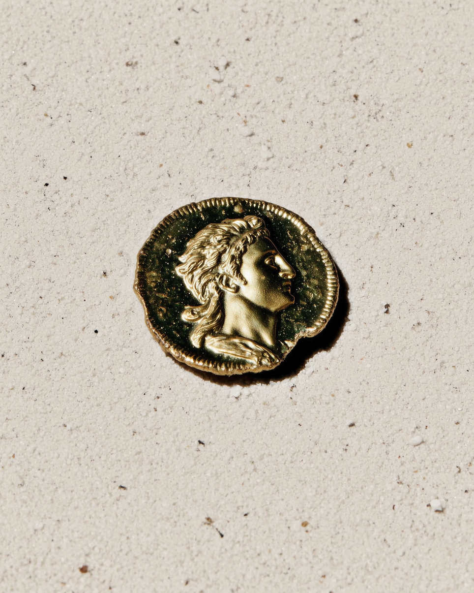 A gold-colored coin bearing a classical profile resembling Lysimachus resting on a textured light surface.