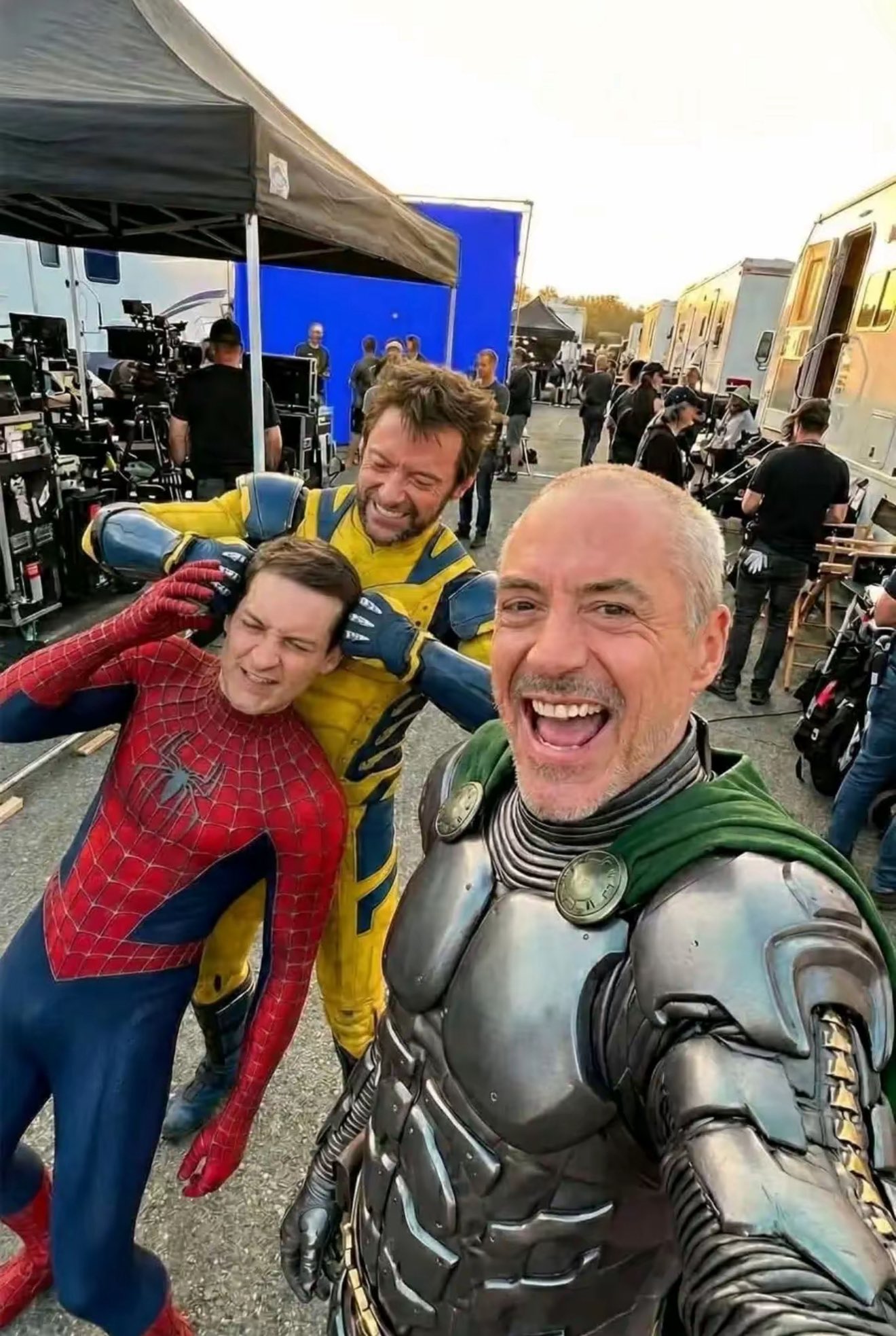 Three men resembling Tobey Maguire, Hugh Jackman, and Robert Downey Jr. in costume on a film set, posed for a selfie.