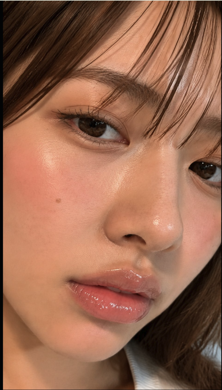 A close-up beauty portrait of a woman, with brown hair and glossy pink lips.