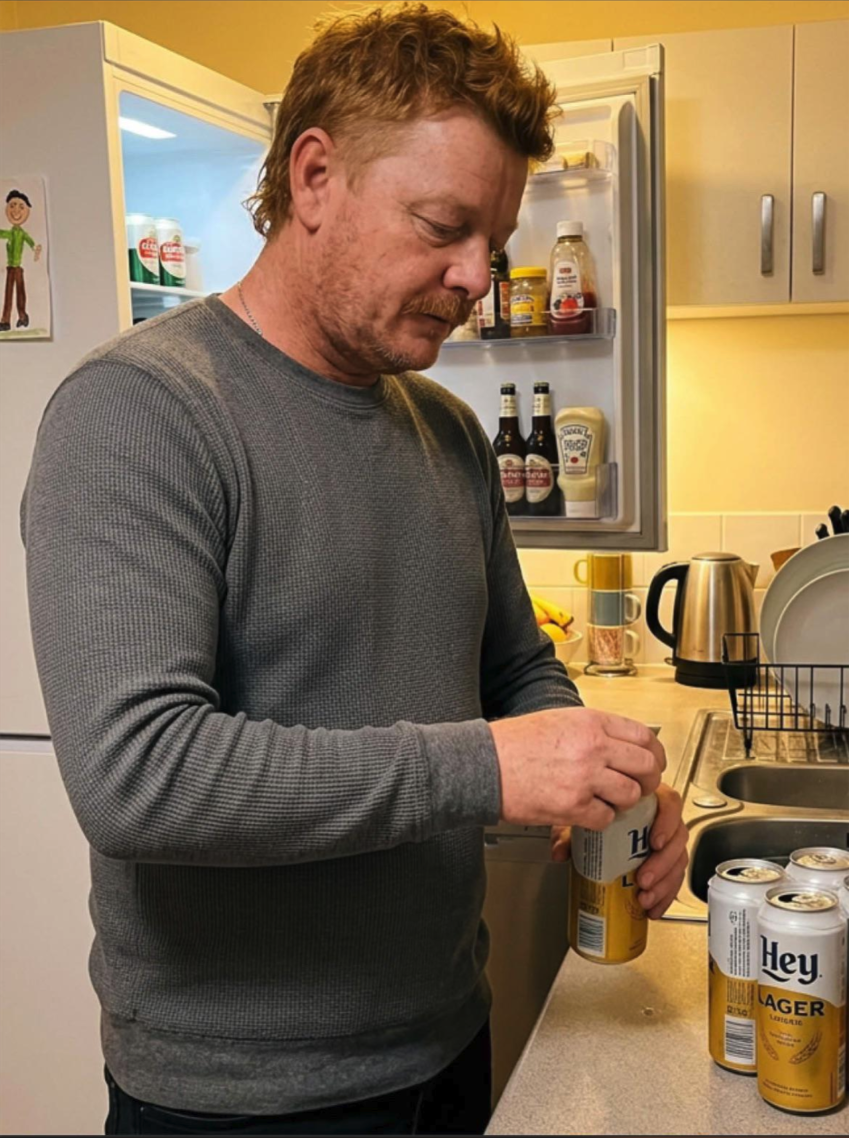 A man in a gray thermal shirt opening a can of beer at a kitchen counter.