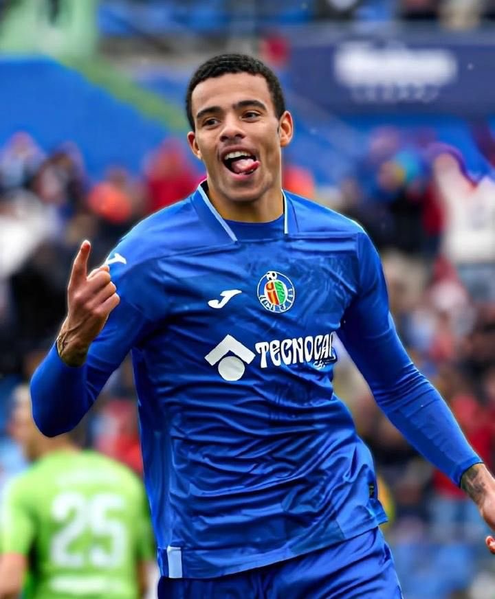 A man resembling Mason Greenwood in a blue Getafe CF kit celebrating on a soccer pitch.