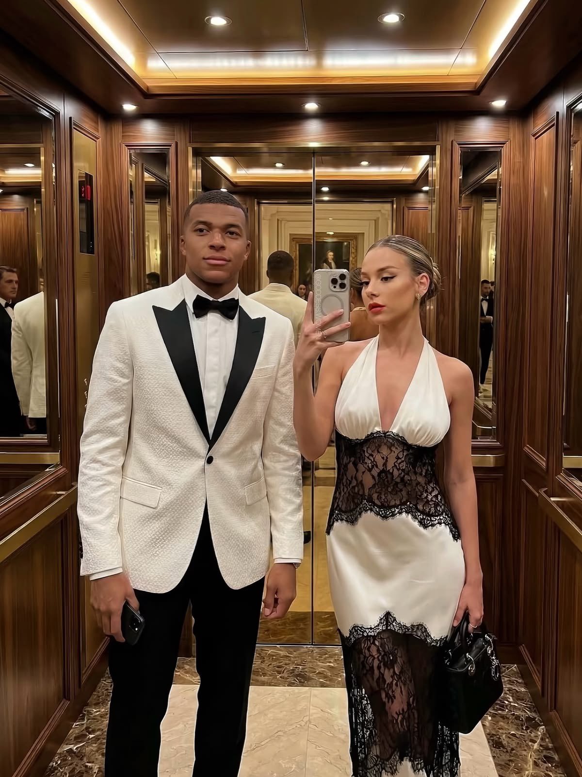 A man resembling Kylian Mbappé and a woman resembling Ester Expósito standing together in a wood-paneled elevator.