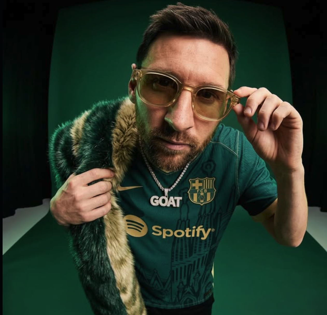 A man resembling Lionel Messi in a green FC Barcelona jersey, amber-tinted glasses, and a 'GOAT' pendant.