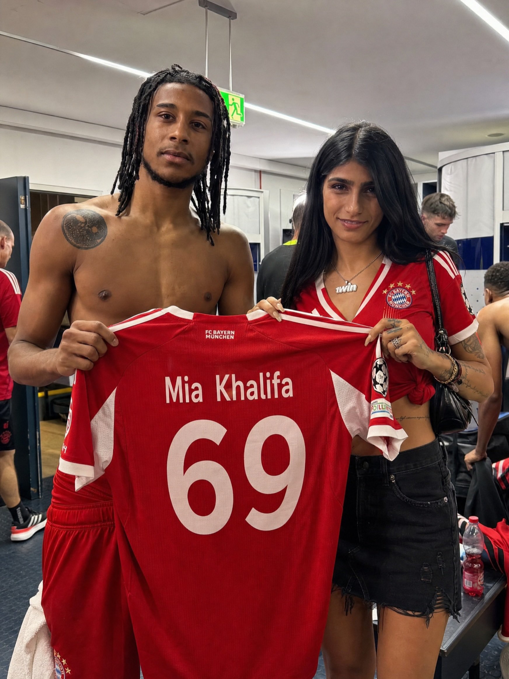 A shirtless man resembling Michael Olise and a woman resembling Mia Khalifa holding a custom Bayern Munich jersey in a locker room.