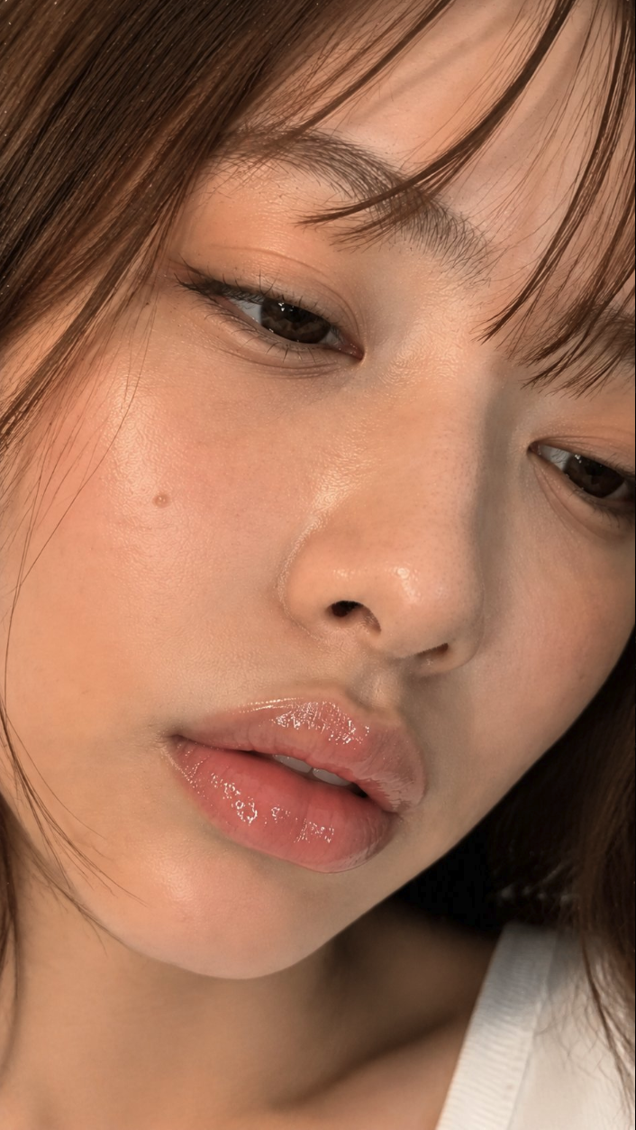 A close-up portrait of a woman, with glossy lips and long dark hair.