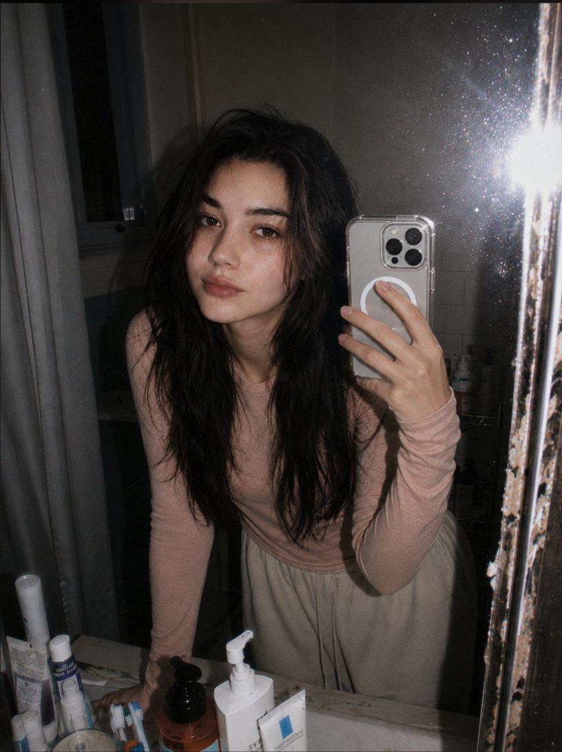 A woman taking a mirror selfie in a bathroom while holding a smartphone.
