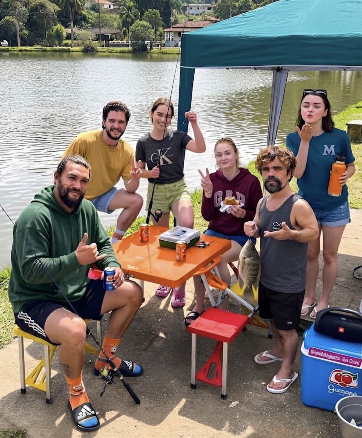 Four people resembling Jason Momoa, Peter Dinklage, Kit Harington, and Emilia Clarke gathered at a lakeside fishing setup.