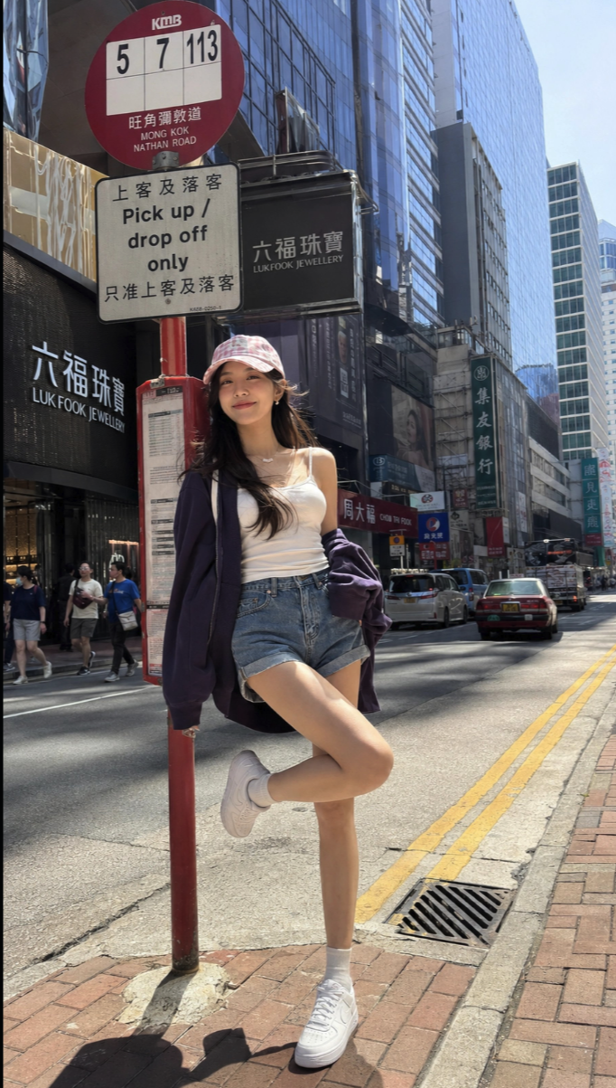 A young woman leaning on a red bus stop pole on a Hong Kong street.