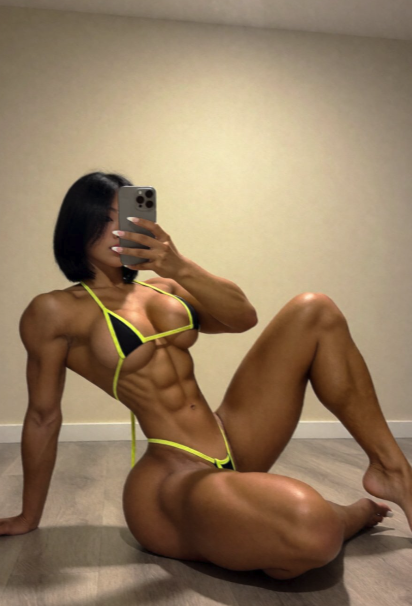 A mirror selfie appearing to show a woman with a muscular physique wearing a black and neon bikini.