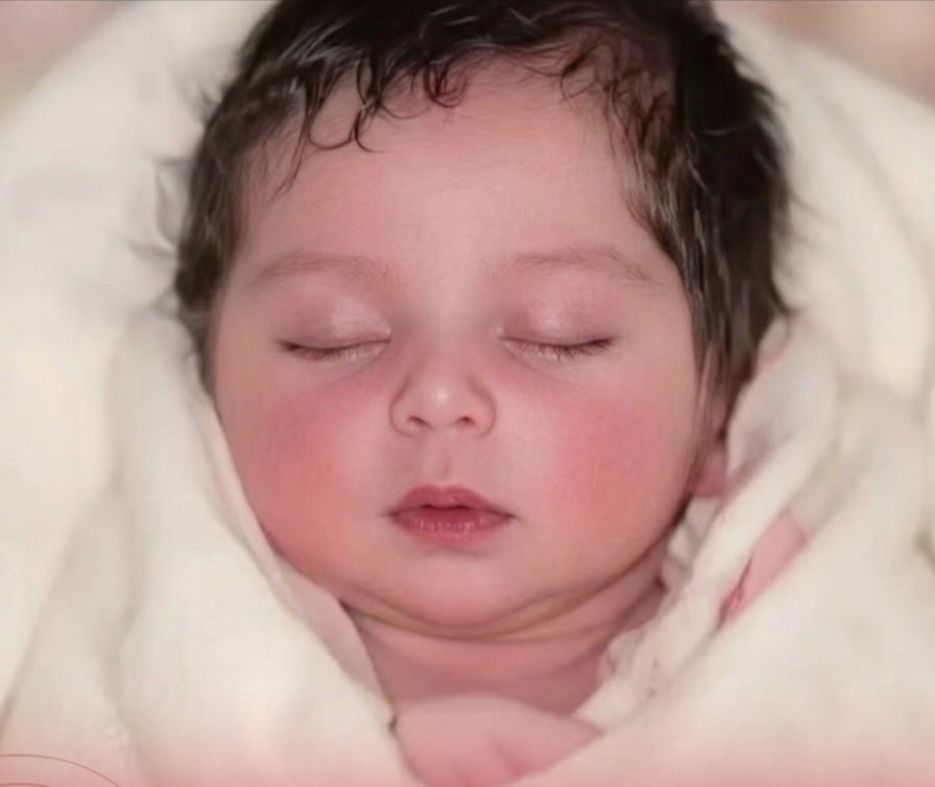 Close-up of a sleeping newborn baby wrapped in a cream blanket.