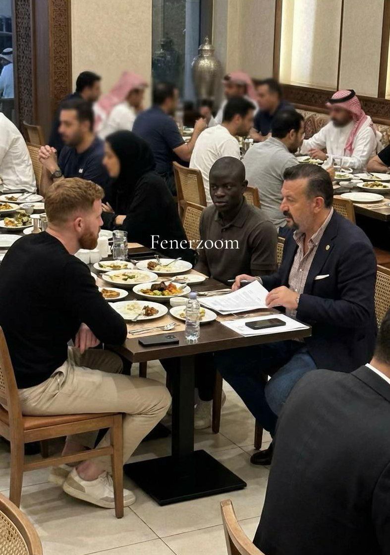 Men resembling N'Golo Kanté and others seated at restaurant tables, with men in traditional Middle Eastern attire in the background.
