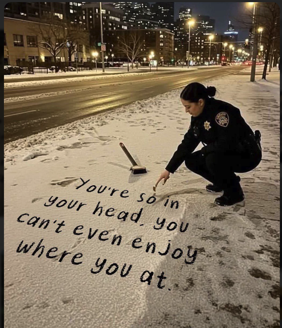 A person in a police uniform crouched at night, writing a message in the snow on a city sidewalk.