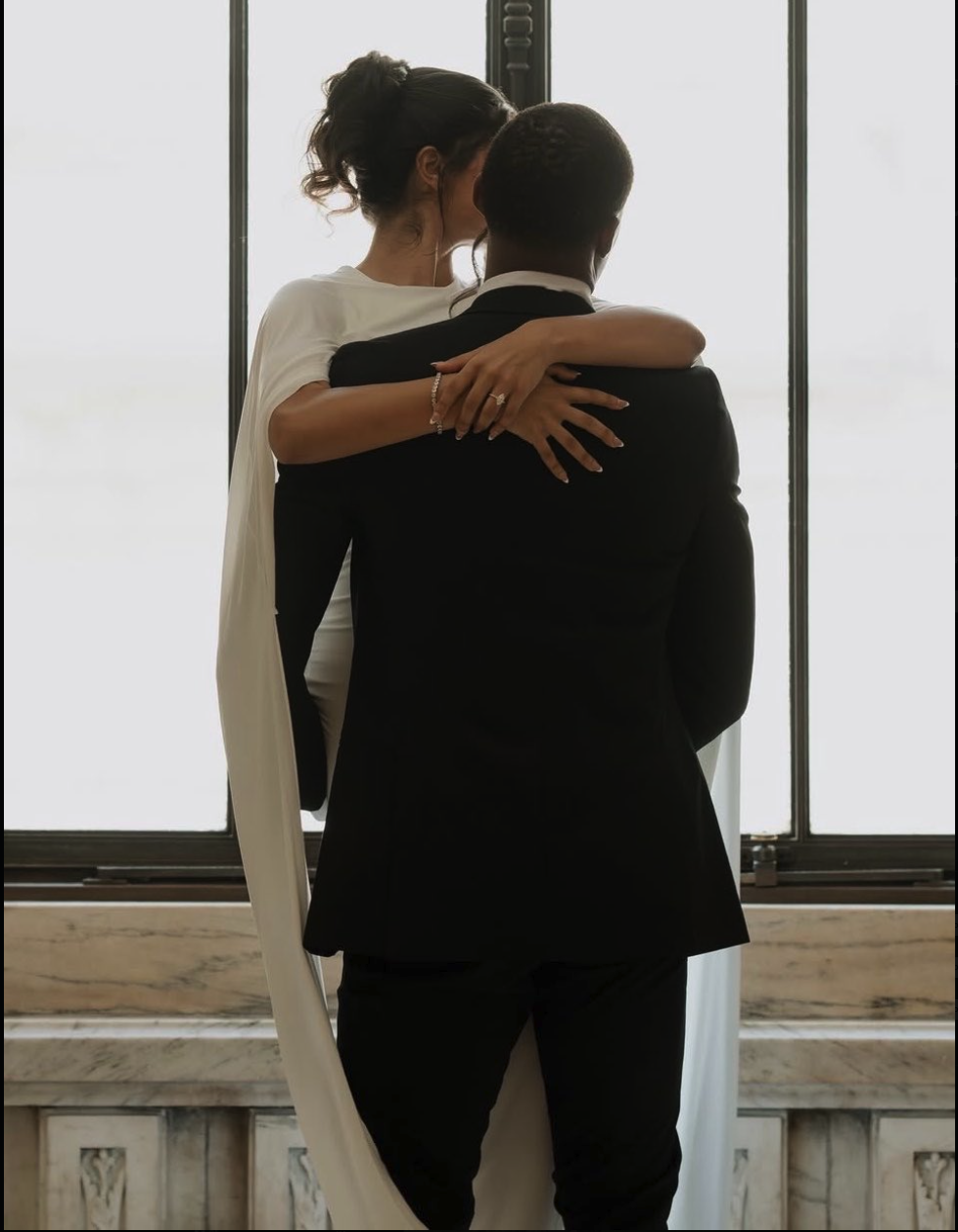 A man resembling Ousmane Dembélé in a black suit embracing a woman in a white wedding dress and veil.
