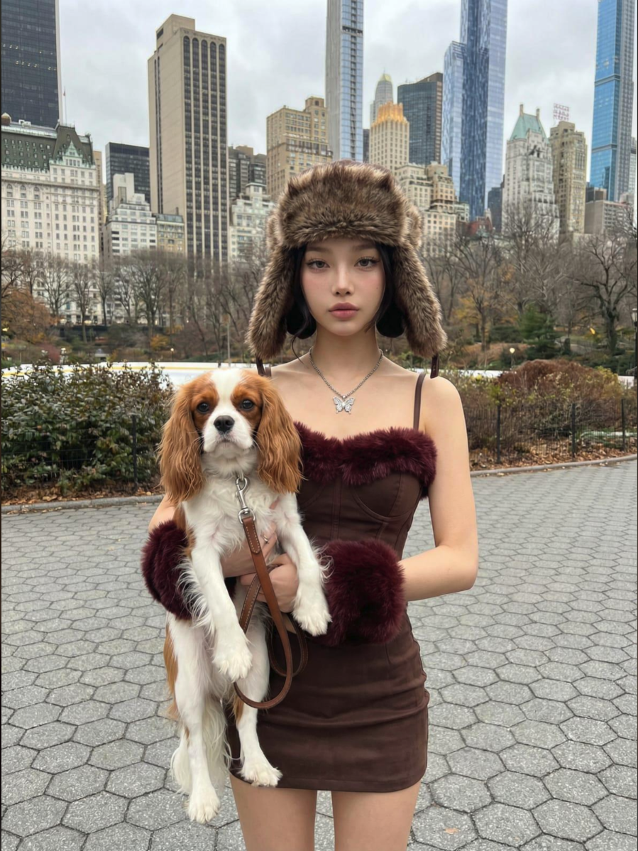 A woman in a fur hat and brown dress holding a Cavalier King Charles Spaniel in Central Park.
